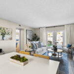 View of living area from the kitchen table. Large doors lead outside, and a short hallway leads to a bedroom