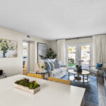 View of living area from the kitchen table. Large doors lead outside, and a short hallway leads to a bedroom