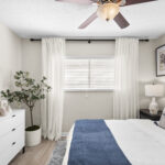 Bedroom with ceiling fan and blinds and curtains over the window