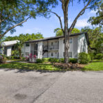 Exterior view of a 2 story apartment building with balconies, large trees, lots of landscaping